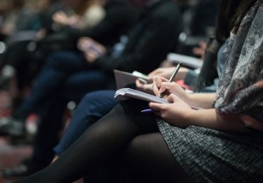 A group of people attending a corporate training conference, diligently writing in their notebooks to improve their business performance.